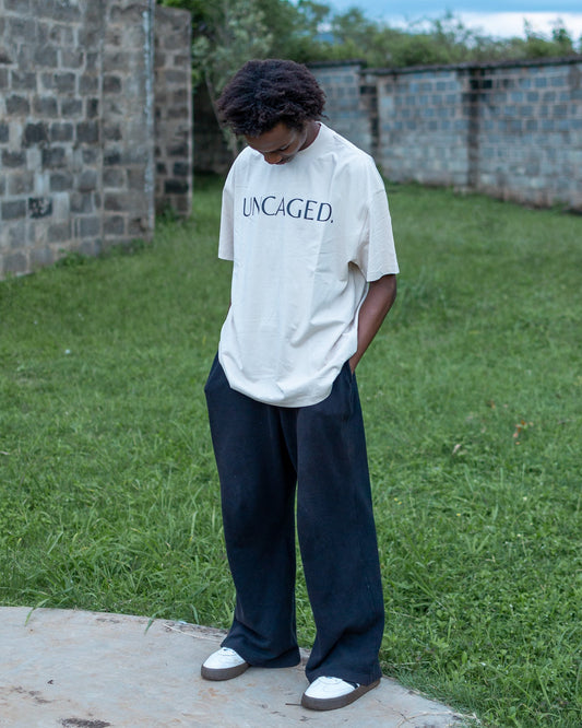 UNCAGED. Origin Tee in beige cream — heavyweight oversized fit with tonal logo print.
