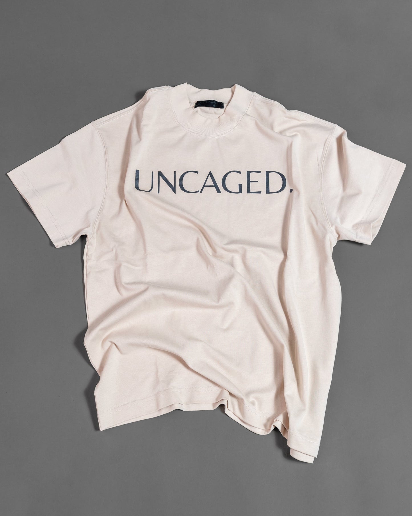 UNCAGED. Origin Tee in beige cream — heavyweight oversized fit, flat lay, tonal logo print.