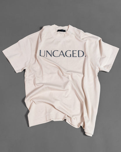 UNCAGED. Origin Tee in beige cream — heavyweight oversized fit, flat lay, tonal logo print.
