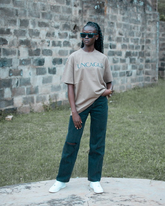 UNCAGED. Origin Tee in taupe brown — heavyweight oversized fit with teal logo print.
