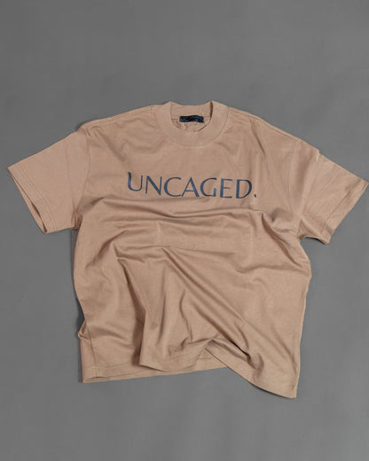 UNCAGED. Origin Tee in taupe brown — heavyweight oversized fit, flat lay, teal logo print.